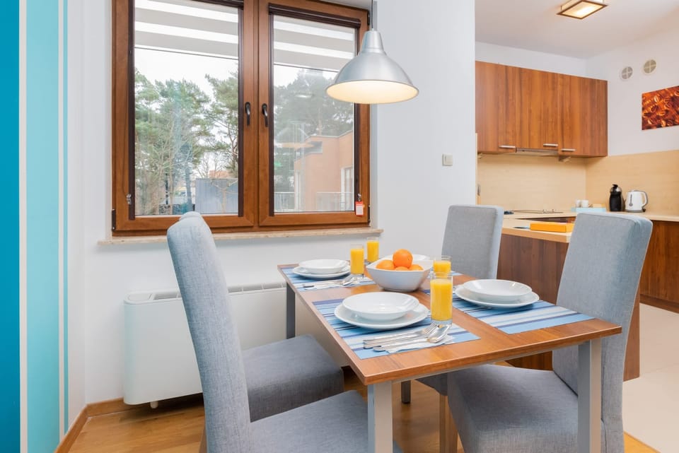  A dining area with a gray dining table and chairs. The room features large windows with bright blue curtains and a light-filled ambiance.