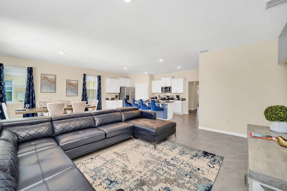 This cozy and sophisticated living room features a leather, wraparound sectional (and built-in chaise lounge), area rug with oceanic undertones, and wall-mounted flat-screen TV.