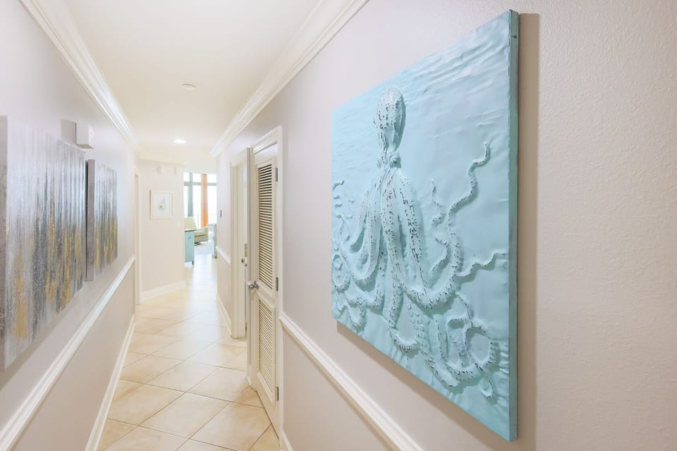 This hallway features a vibrant octopus artwork and leads to a welcoming living area with natural light and a beach view
