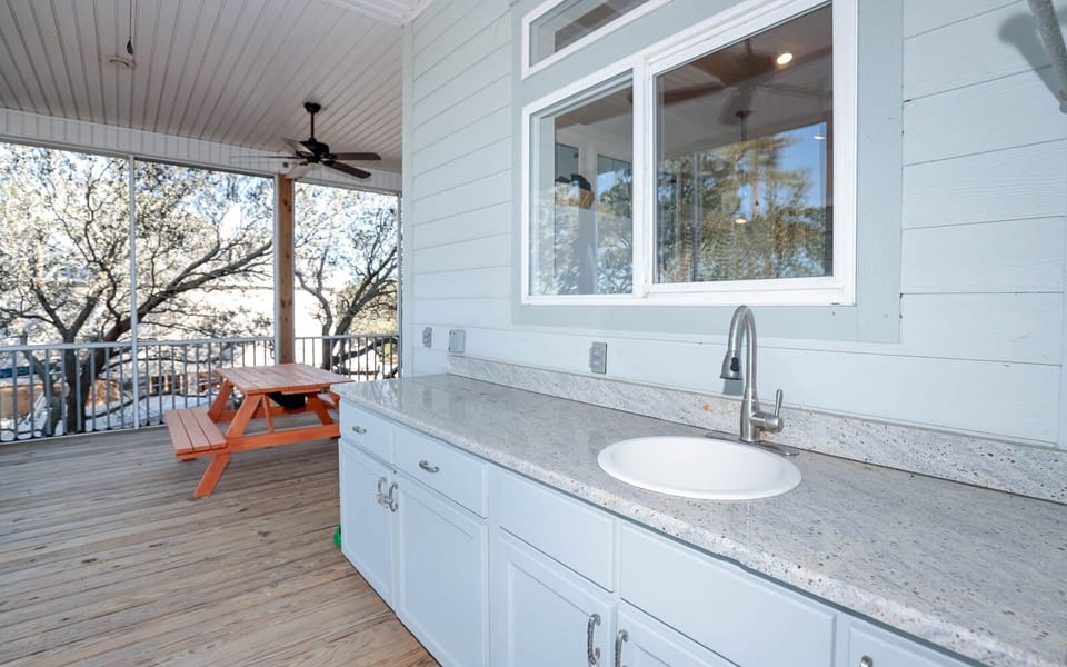 This outdoor space features a sleek countertop with a sink, complemented by a picnic table and a view of lush trees