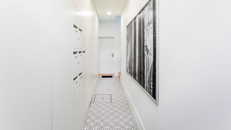 Walk through a chic and serene corridor that reflects the modern elegance of your stay, leading you to your private retreat within this beautifully designed apartment. The distinctive patterned floor tiles and large artwork add sophistication to the strea