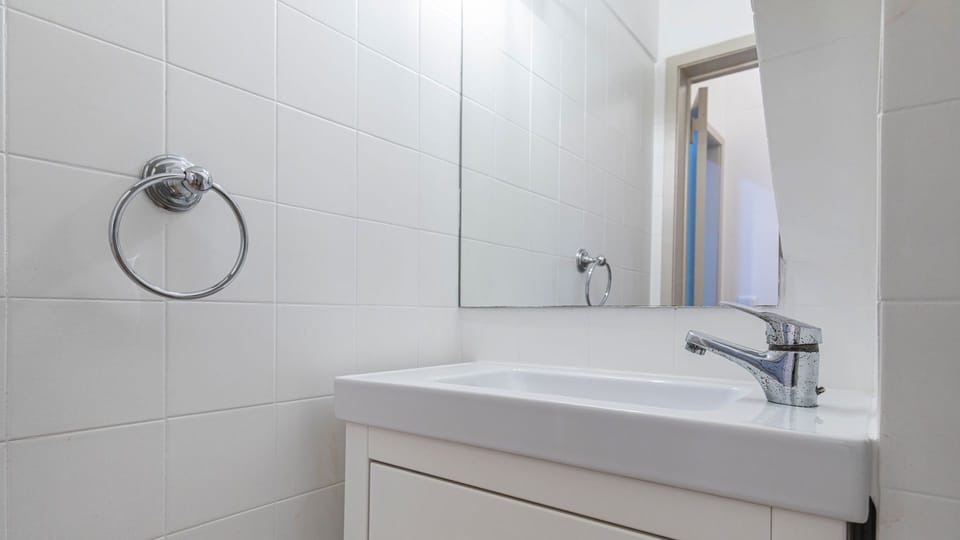This pristine, all-white bathroom provides a serene and immaculate space to refresh, featuring a contemporary vanity and a large mirror.