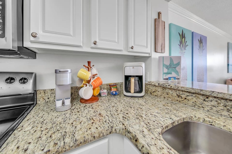 Start your morning with fresh coffee from your fully equipped kitchen, featuring granite counters and cheerful coastal artwork.