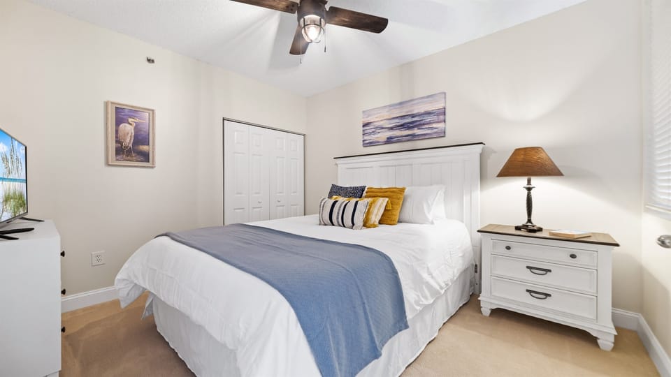 This well-appointed 2nd guest room features a queen-size bed with a decorative headboard, crisp white bedding, stylish nightstand with lamp, and tile flooring for easy maintenance.