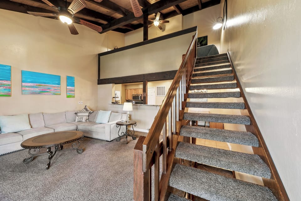 Relax in your spacious living room with soaring beamed ceilings and comfortable seating, while the open-concept design connects you to the full kitchen above.