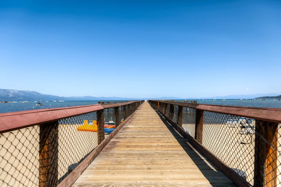 Wooden boardwalk extends over pristine beach with mountains and azure waters creating a stunning coastal setting.