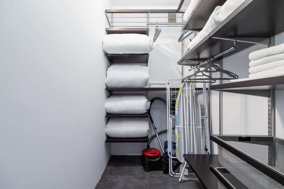 A compact storage room with shelves neatly organized with household essentials like linens and cleaning supplies.