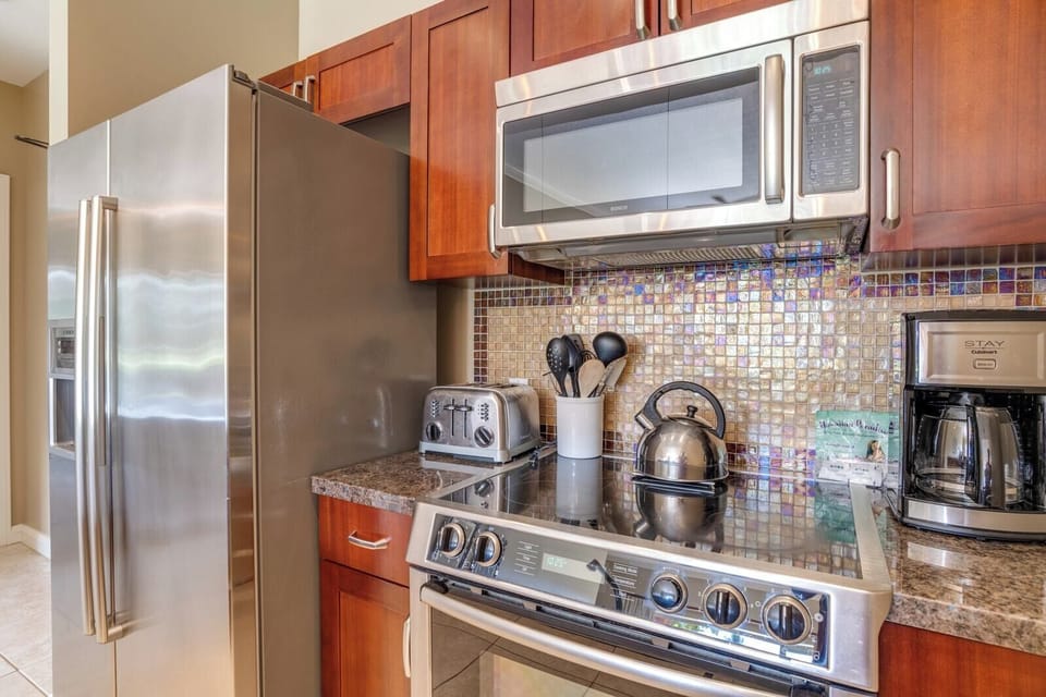 Stainless steel appliances and mosaic backsplash enhance cozy kitchen corner.
