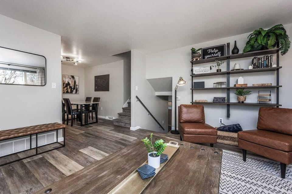 - Rustic wood coffee table anchors a living room full of charm and character
- Open layout flows to the dining area and stairway creating an airy vibe
- Mix of textures from leather wood and steel offers depth and warmth

