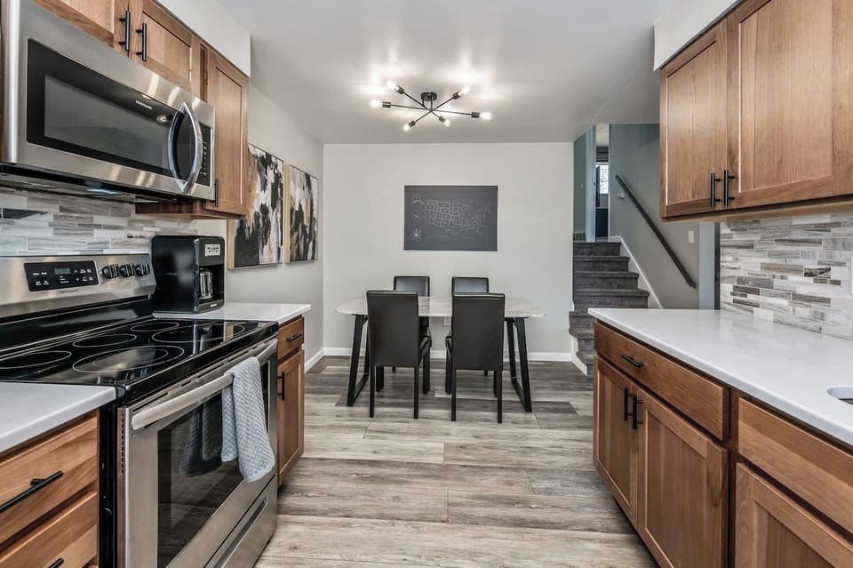 - Stylish kitchen with wood cabinets stainless appliances and sleek countertops
- Dining area for six beneath a bold light fixture and gallery wall accent
- Warm flooring and open sightlines create flow and function throughout

