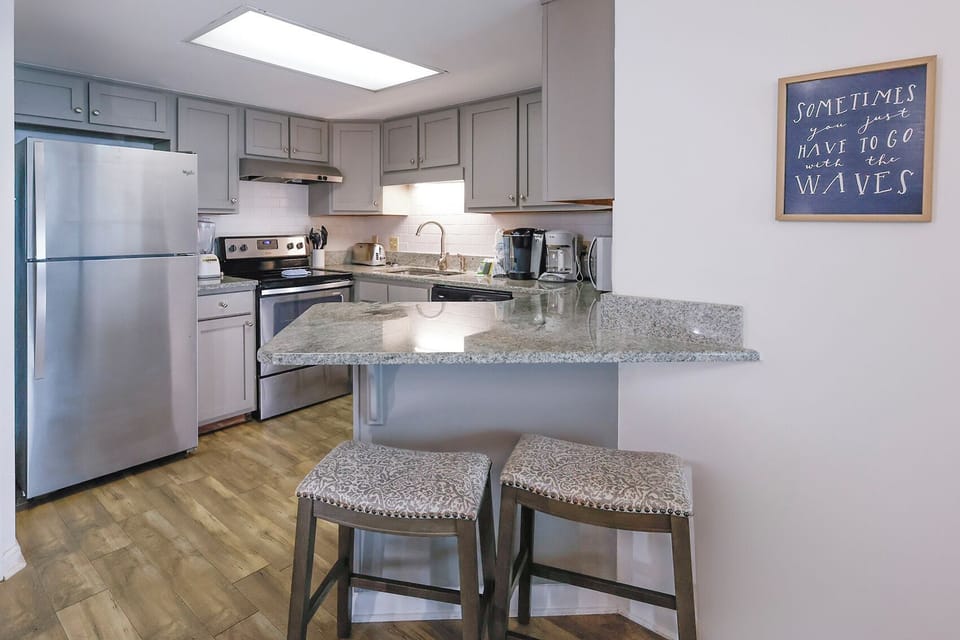 A well-equipped kitchen features stainless appliances, granite countertops, and a cozy bar area with two upholstered stools