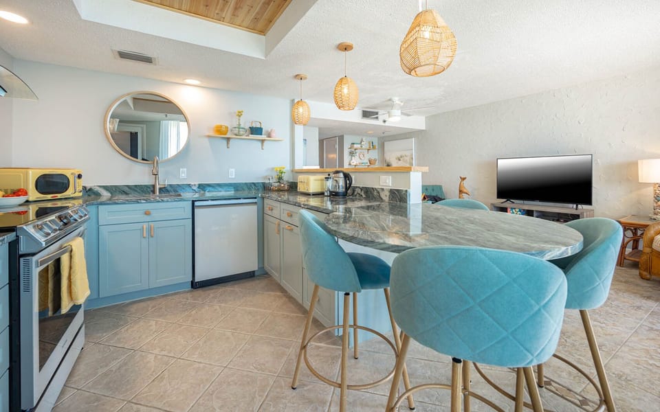 The open kitchen design features smart appliances, a stylish countertops, and a  dining area with turquoise bar stools