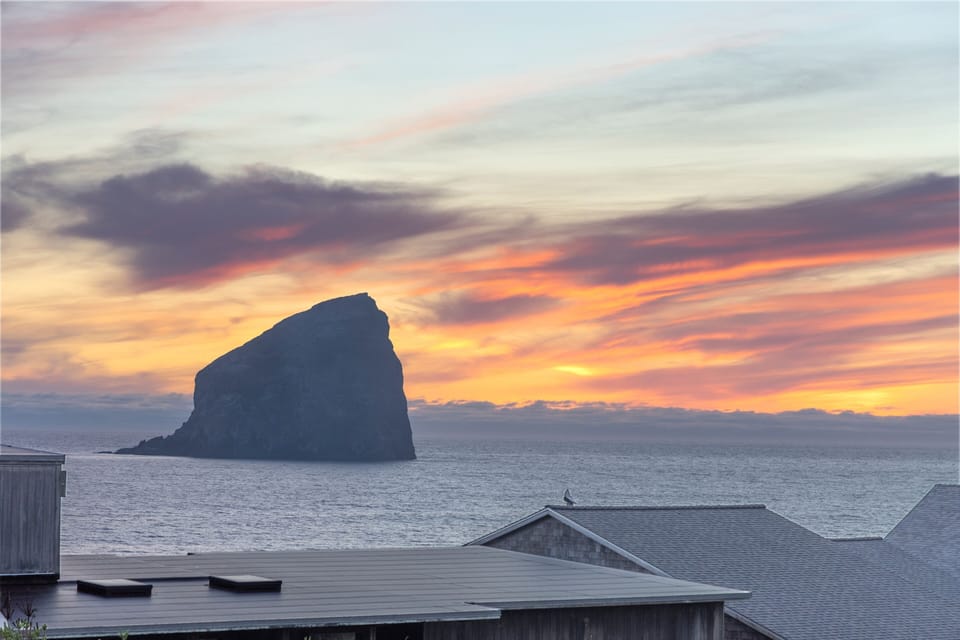 Dramatic sunset paints the sky in vibrant hues over the iconic Haystack Rock and Pacific Ocean coastline.