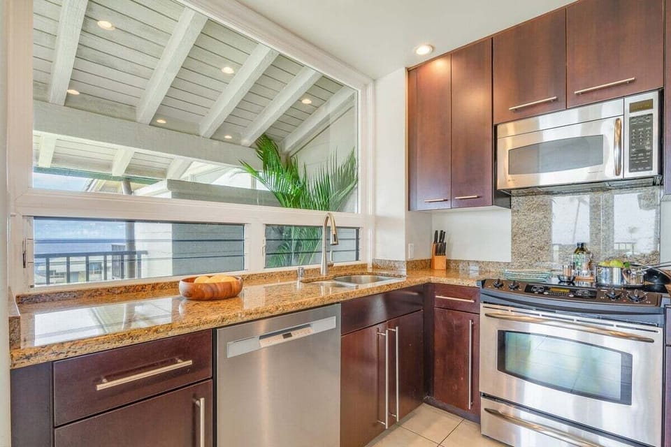 Bright open kitchen with vaulted ceilings, granite counters, and bar seating that enhances the airy feel of this island‑inspired space.