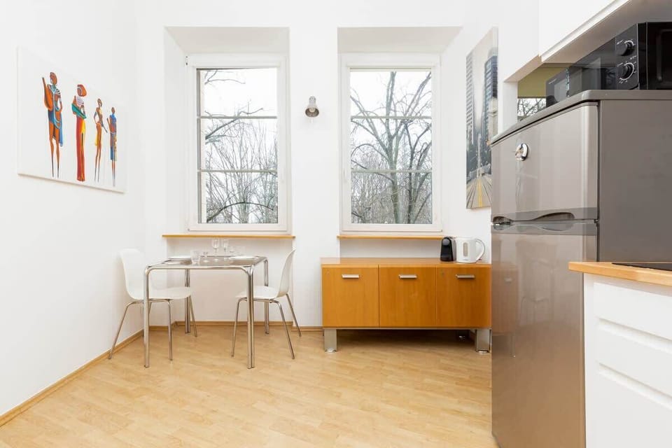 A bright dining area with a wooden table and chairs, next to a wide window.
