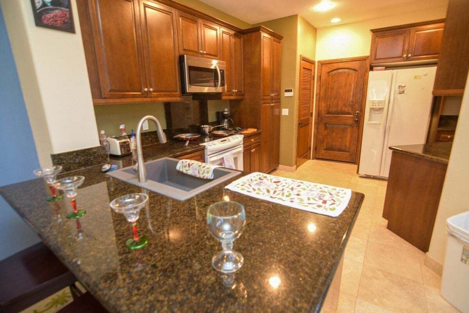 This gourmet kitchen features wood cabinets, granite countertops, full-size modern appliances, and an elevated breakfast bar with high-top seating — perfect for margaritas and mingling while meals cook .