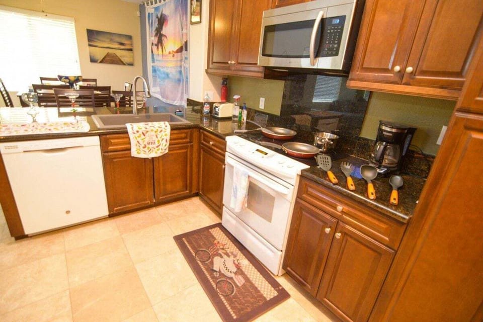 This sleek kitchen features stainless steel appliances, granite countertops, beautiful wood cabinets, and an island with three bar stools — perfect for entertaining while cooking .