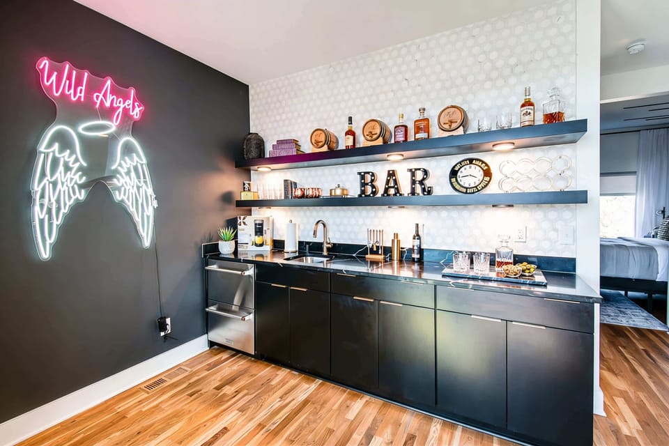 The 'Wild Angels' neon glows above a built-in wet bar stocked and ready, setting the tone for game room nights that stretch until dawn. Book your stay with Misfit Homes to lock in this party headquarters