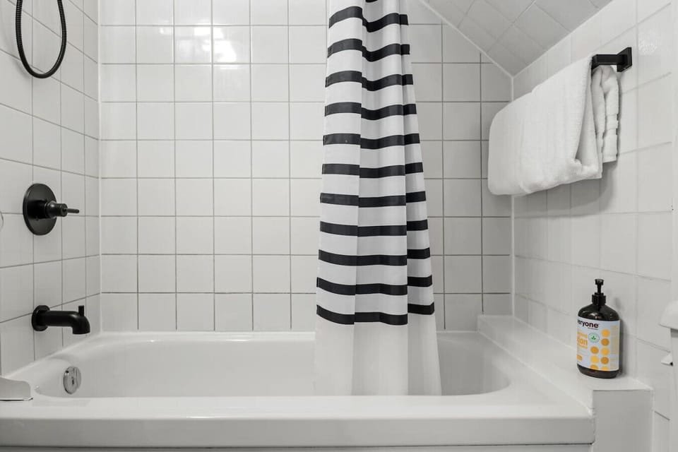 Bathtub with black hardware, striped shower curtain, and provided toiletries.