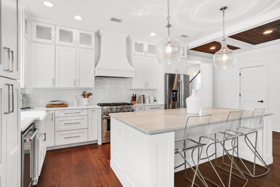 You'll love preparing meals in this stunning white kitchen with marble countertops, modern appliances, and elegant pendant lighting.