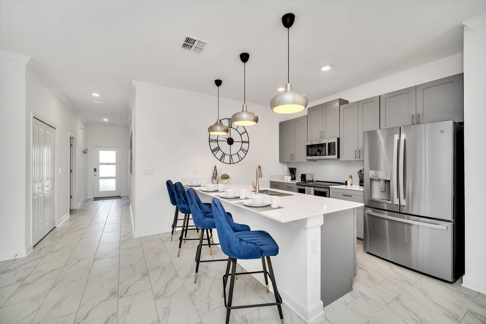 Modern kitchen of the townhouse in Kissimmee Florida - Features a stylish counter table accompanied by sleek blue high chairs - A contemporary and inviting casual dining space within the kitchen - Stainless steel appliances