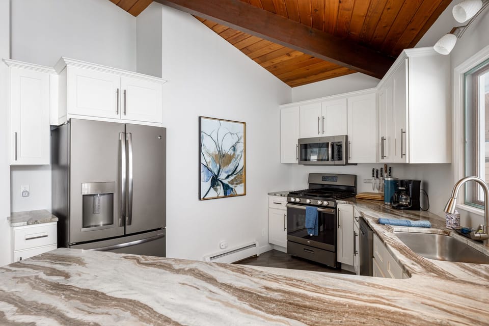 Bright kitchen w/ L-shaped counter, stainless appliances & vaulted wood ceiling.
