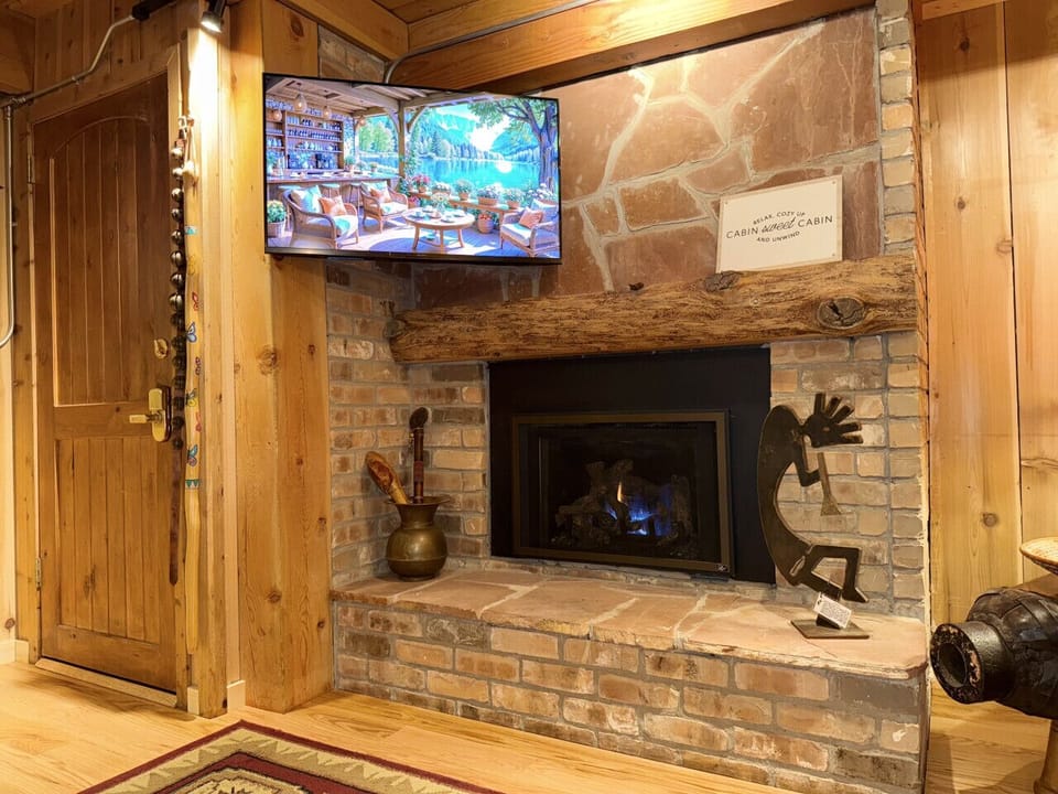 Living room with fireplace and smart TV” – RECAPTION: “Fireplace for warmth, Kokopelli for charm, Smart TV for when you’ve given up on talking to each other
