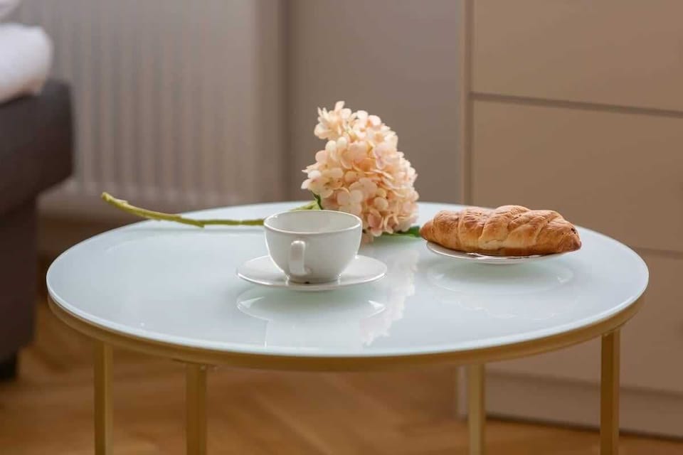 A dining table setup with a plate of croissants, a cup of coffee, and decorative flowers.

