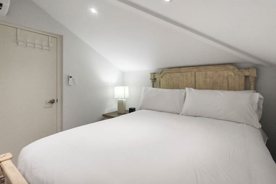 Bedroom 4 | Restful guest bedroom tucked under a sloped ceiling, showcasing a rustic wooden headboard, soft lighting, and plush linens.