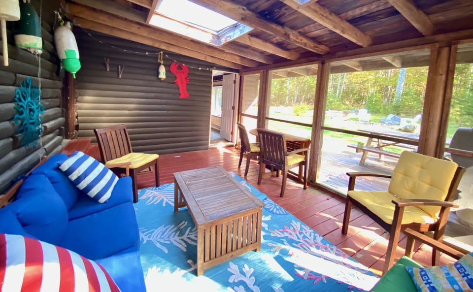 View from screened porch toward deck, fire pit, and bedroom through white door.