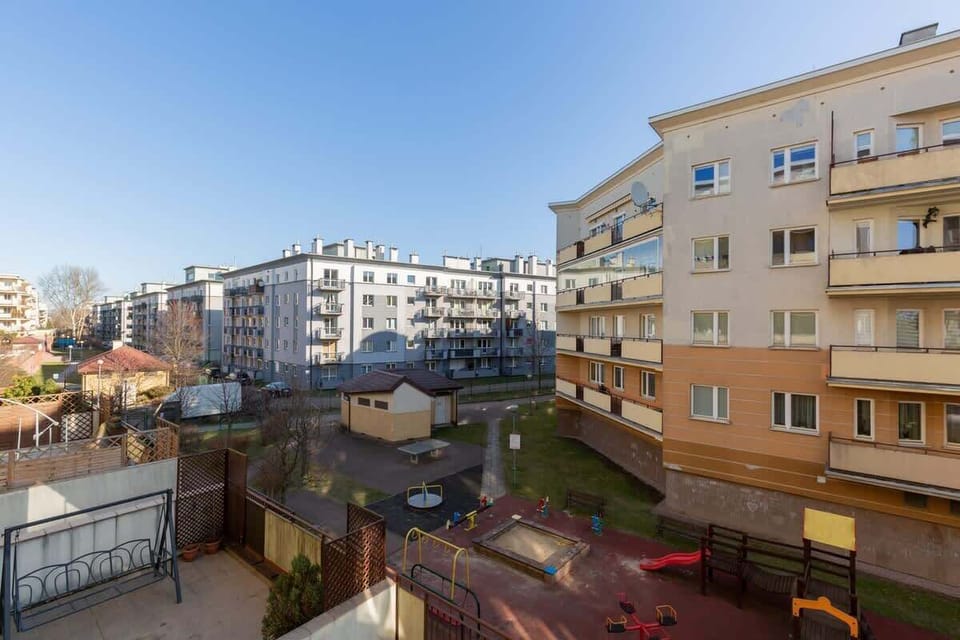 A balcony view overlooking modern apartment buildings, landscaped areas, and an open sky.