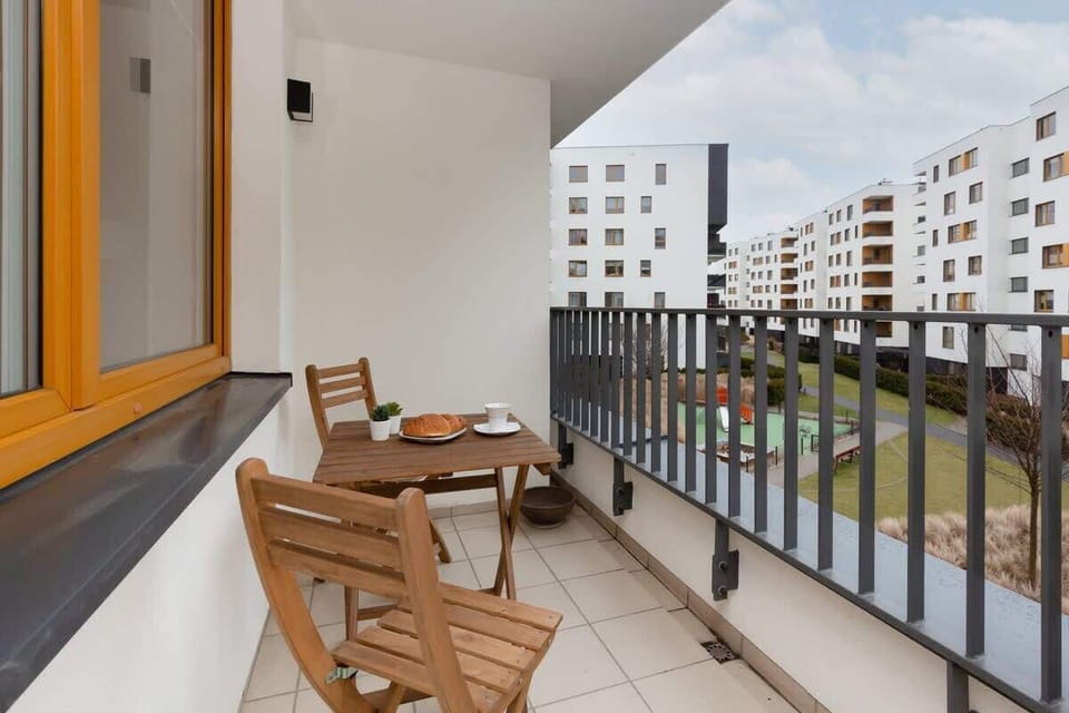 A spacious balcony with wooden flooring and outdoor furniture, offering views of a residential complex and green spaces.