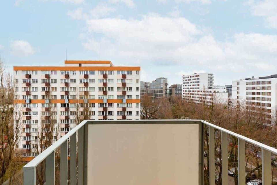 A balcony with a metal railing offering a view of nearby apartment buildings and trees under a clear sky.