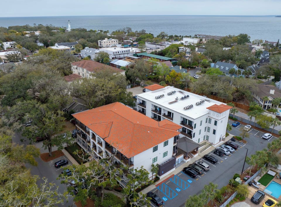 Aerial view showcasing the property's Mediterranean-style architecture with terracotta roofing, convenient parking facilities, and proximity to the waterfront and charming coastal town.