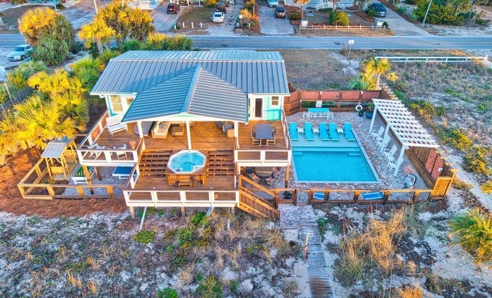 Aerial view of beachfront vacation rental featuring swimming pool, hot tub, and multi-level deck surrounded by tropical palms.