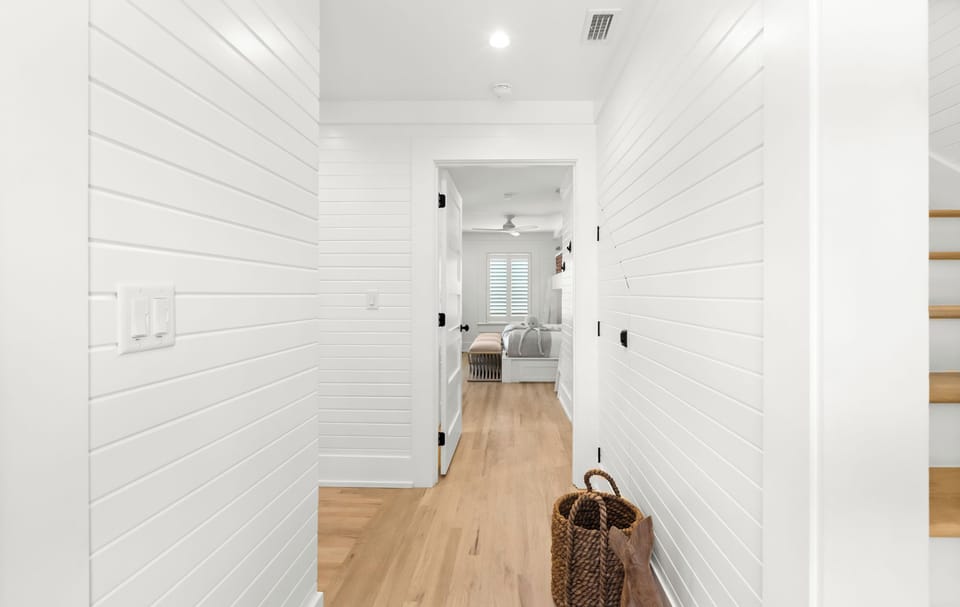 Step into your serene hallway with coastal charm—white shiplap walls, warm wood floors, and a glimpse of your cozy bedroom ahead inviting you to settle in.