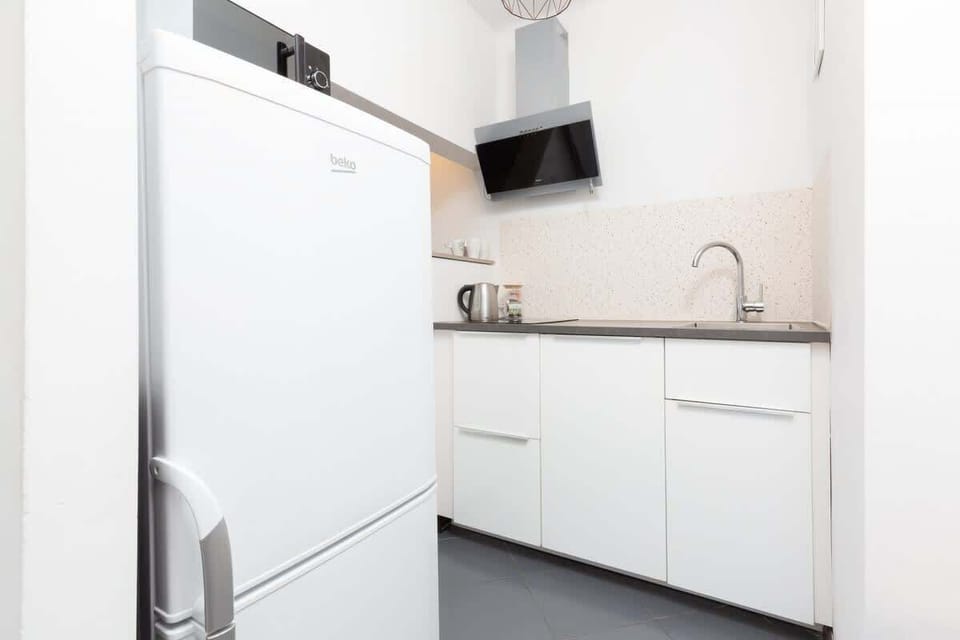 A modern kitchen area with white cabinets and stainless steel appliances. The design is sleek and functional, emphasizing clean lines.