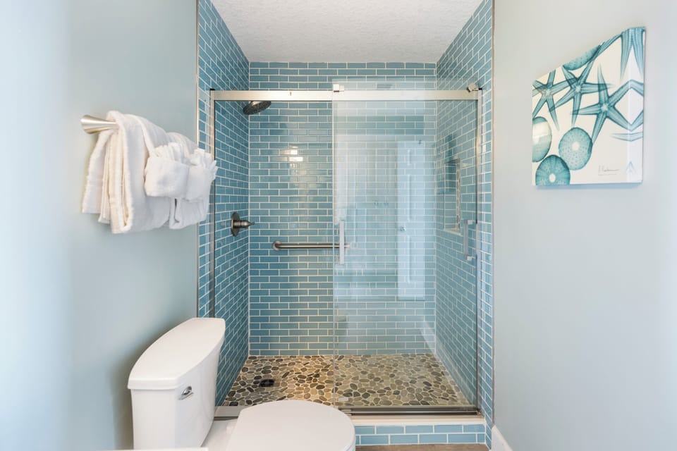 Refresh in your beautifully tiled shower with calming blue subway walls and natural stone flooring, complete with fluffy towels waiting.