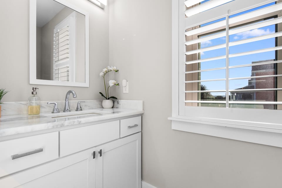Refresh in this elegant bathroom with marble counters and bright natural light streaming through plantation shutters.