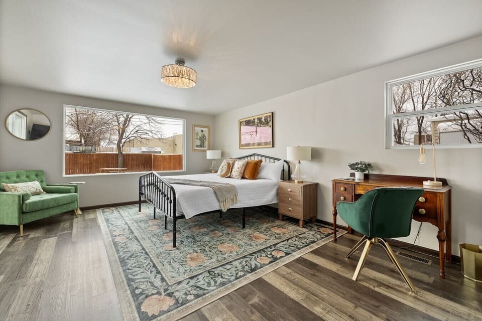 Spacious master bedroom with a cozy queen bed, dedicated workspace, comfy couch, and a large window for natural light.