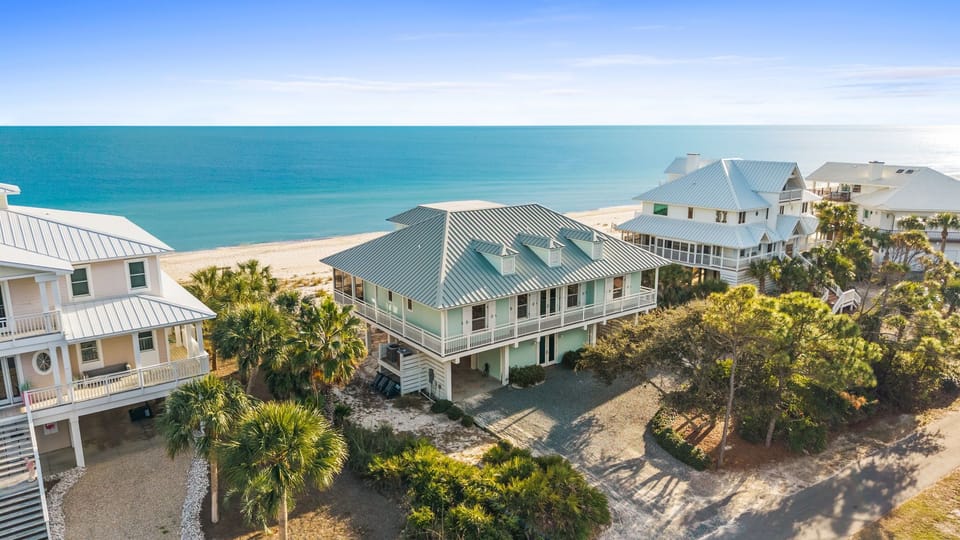 Aerial view of beachfront vacation homes nestled among palm trees, just steps from pristine sandy shores and turquoise waters.
