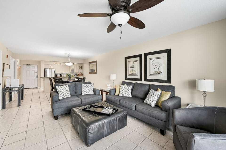 Relax in this spacious living room with plush gray sofas, modern décor, and an open layout connecting to your fully-equipped kitchen.