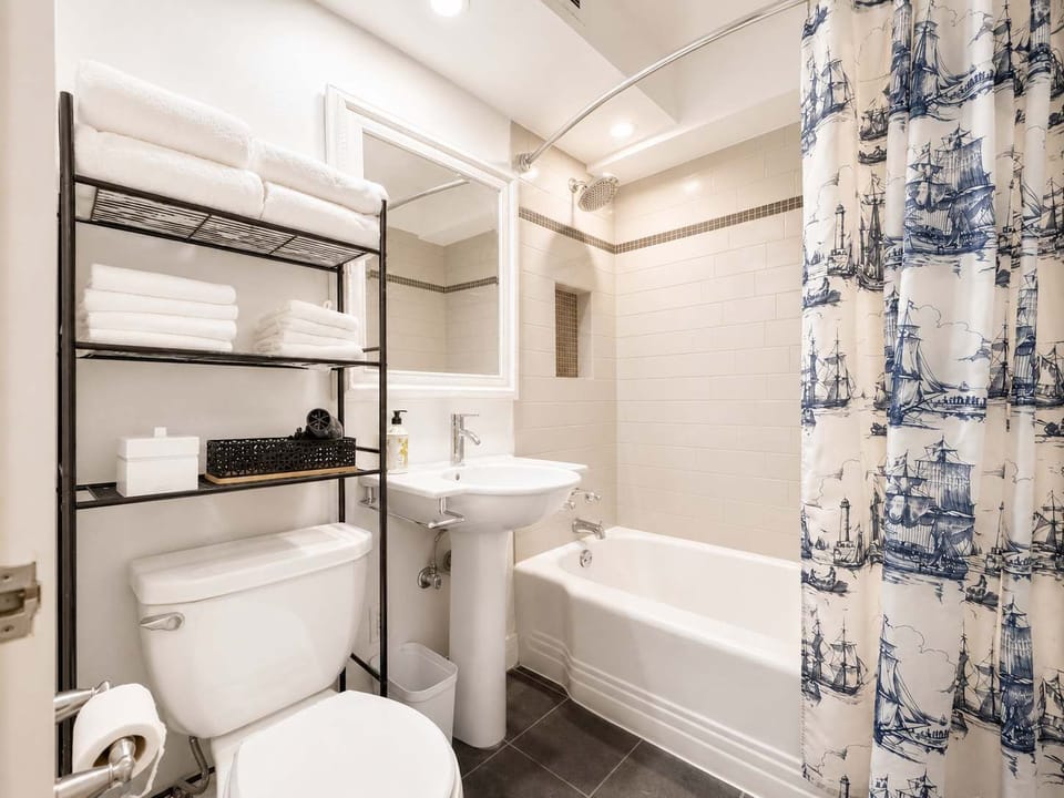 Refresh in a bright, spotless bathroom equipped with a full tub, pedestal sink, and convenient over-the-toilet storage.