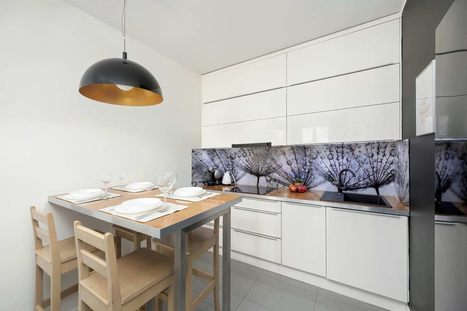 Kitchenette with white cabinets, wooden table and decorative wall panel.