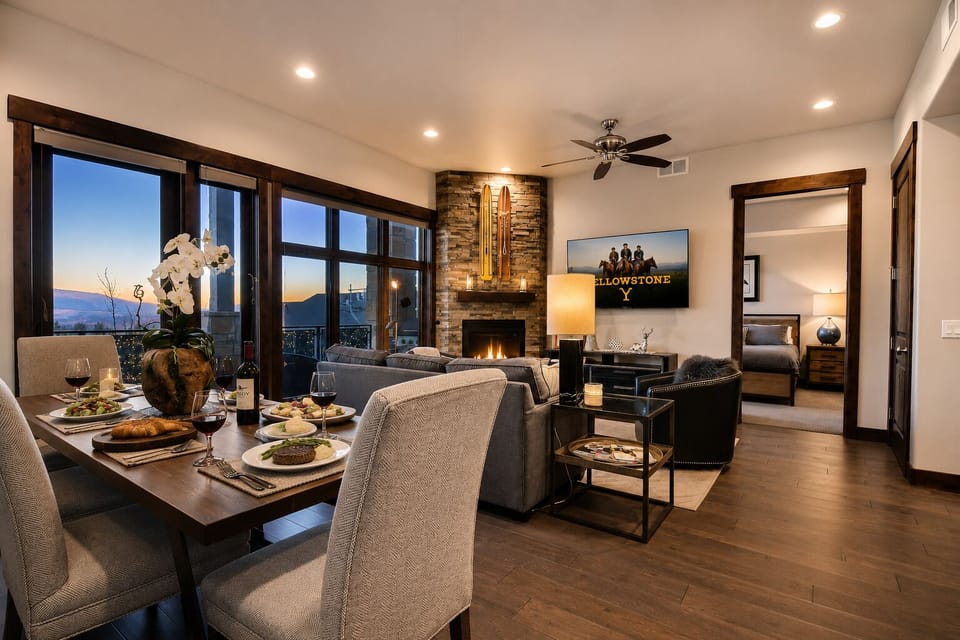 Unwind in this inviting open-concept living and dining area with a stunning stone fireplace, elegant furnishings, and breathtaking mountain views at sunset. Your perfect retreat awaits.