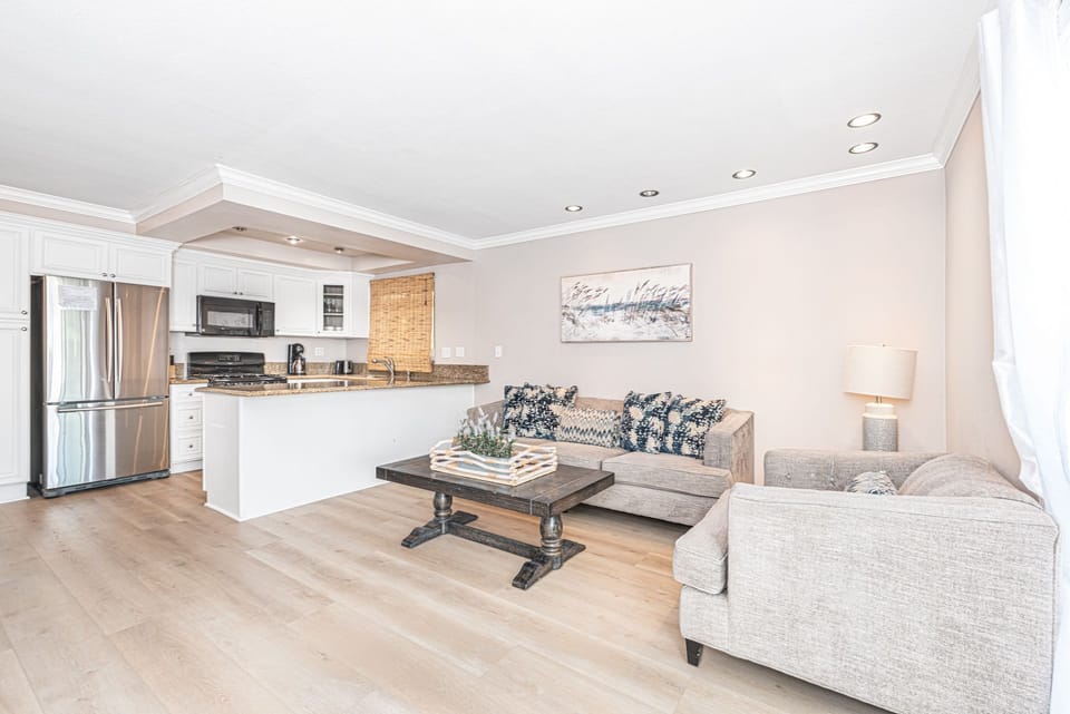 The main living area includes a sofa and love seat, smart TV, and dining table with seating for 6, and doors that open out to the front patio. The fireplace has been permanently disabled.
                