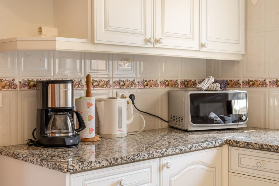 A well-equipped kitchen featuring light granite countertops and white cabinetry. The counter holds modern appliances like a coffee maker, an electric kettle, and a microwave, ready for daily use.