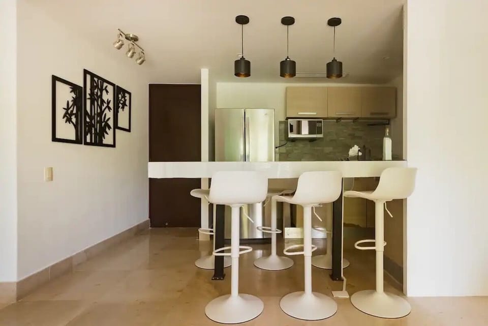Puerta de la entrada. Cocina y barra con 6 sillas.