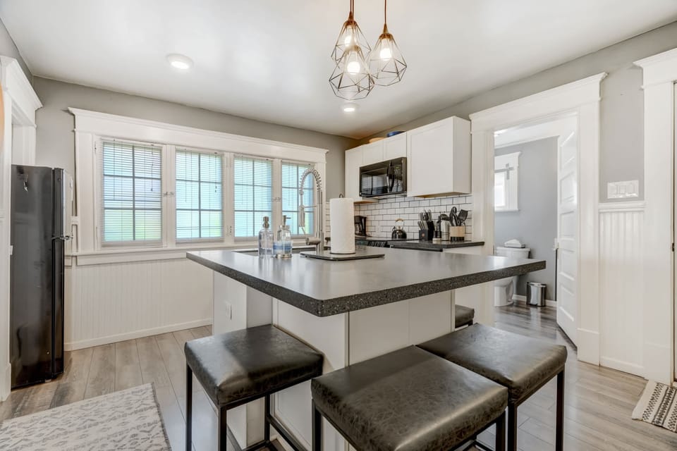 Light-filled kitchen with a breakfast bar for two—pull up to the cushioned stools, prep on the wraparound counter, and enjoy clean white cabinetry plus big windows.