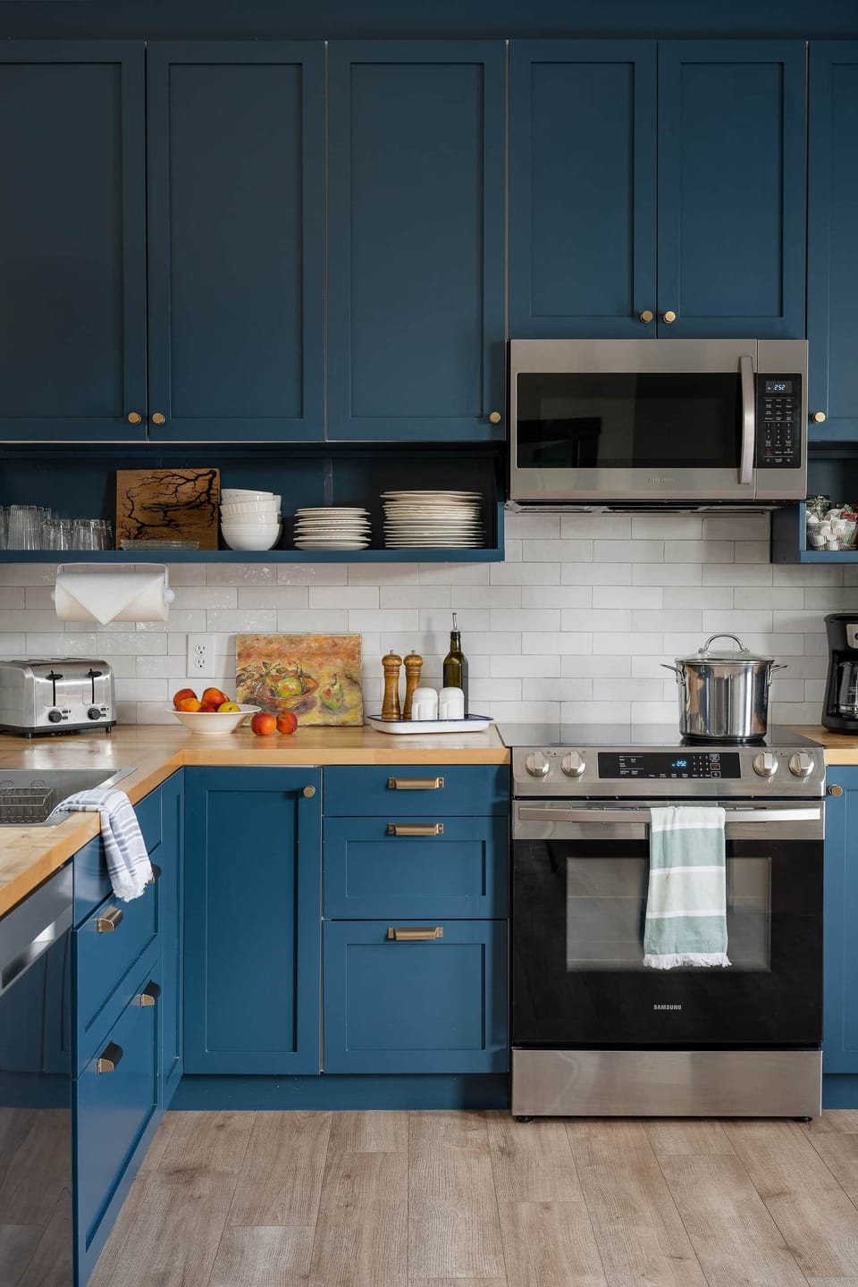 Blue kitchen with a stainless range and microwave dishware on open shelves and wood countertops.